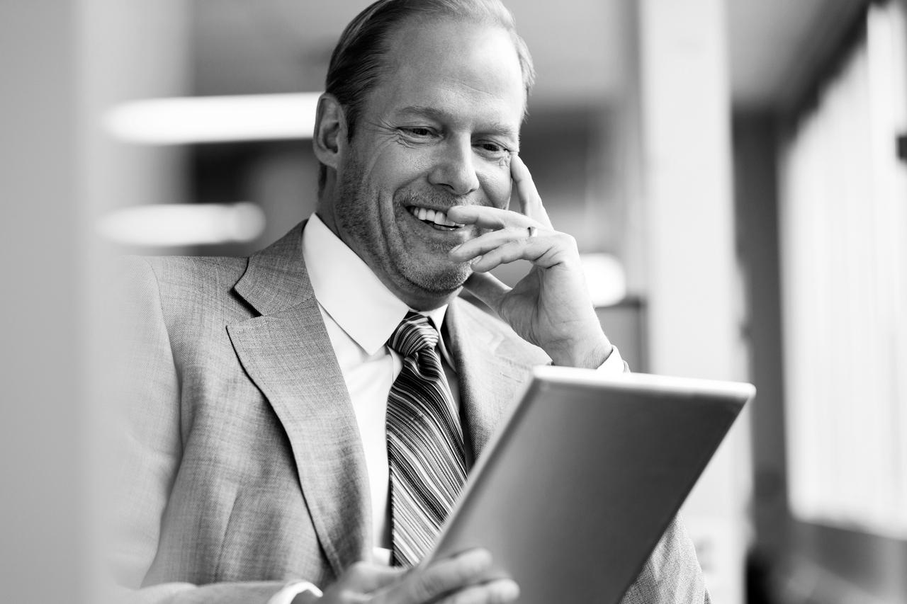 Middle-aged business man smiling and using tablet computer in office