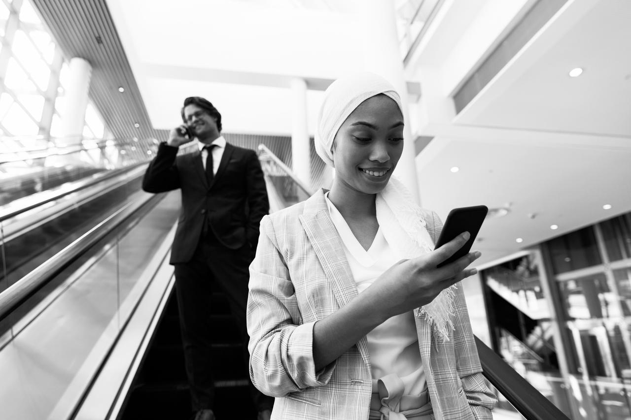 A black and white photo of a businessman and woman on an escalator.
