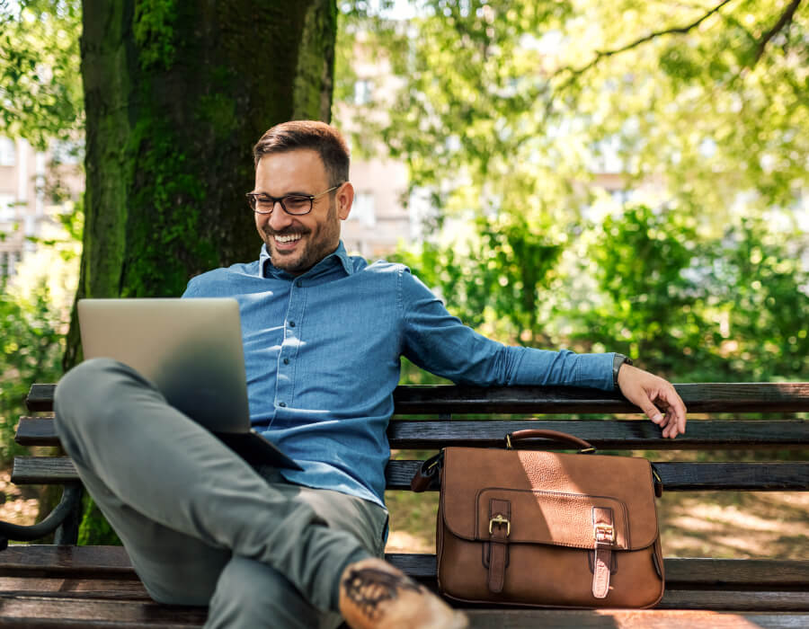 A professional businessman sitting in the park working on his laptop.