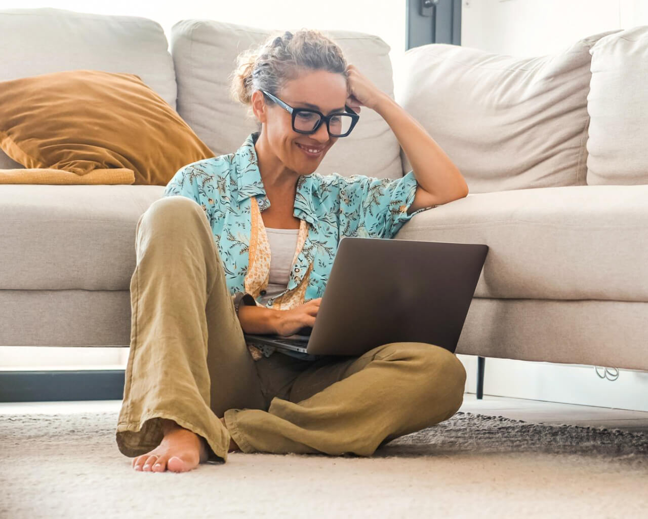 A woman sitting on the floor working on her laptop.