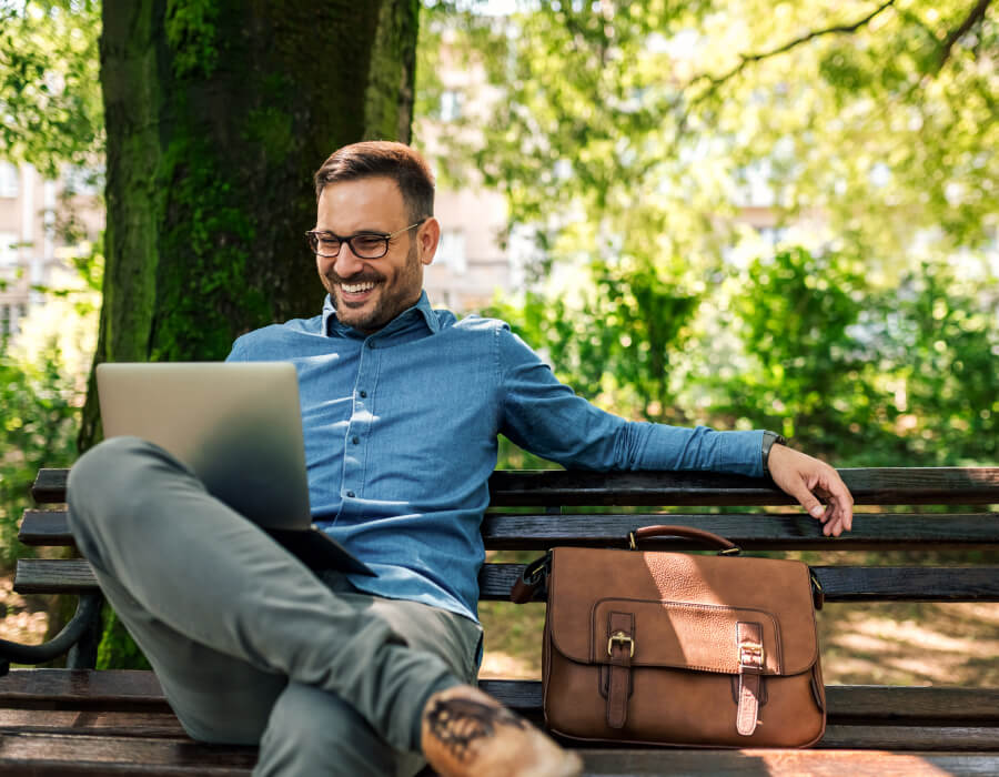 Man sitting on park bench working on computer