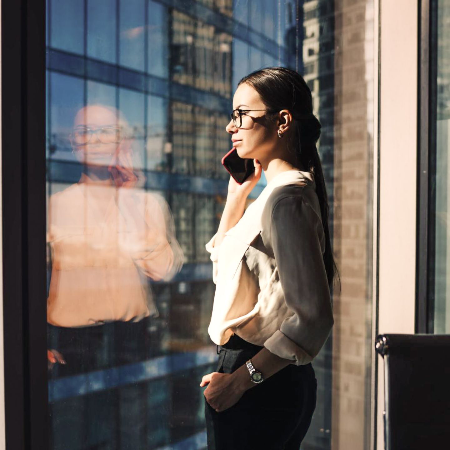 A business professional looking out the office window while talking on her mobile phone.