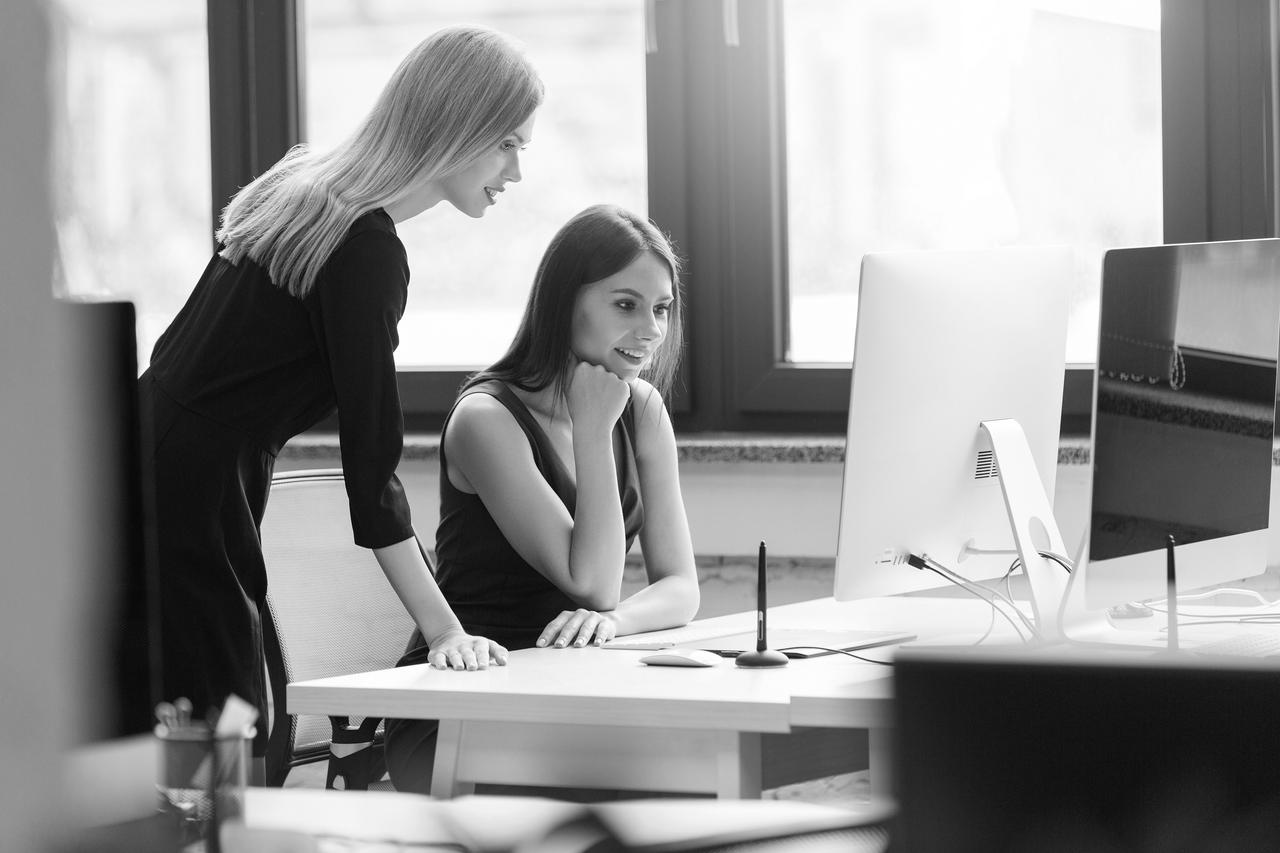 Two women in an office setting looking at a computer screen