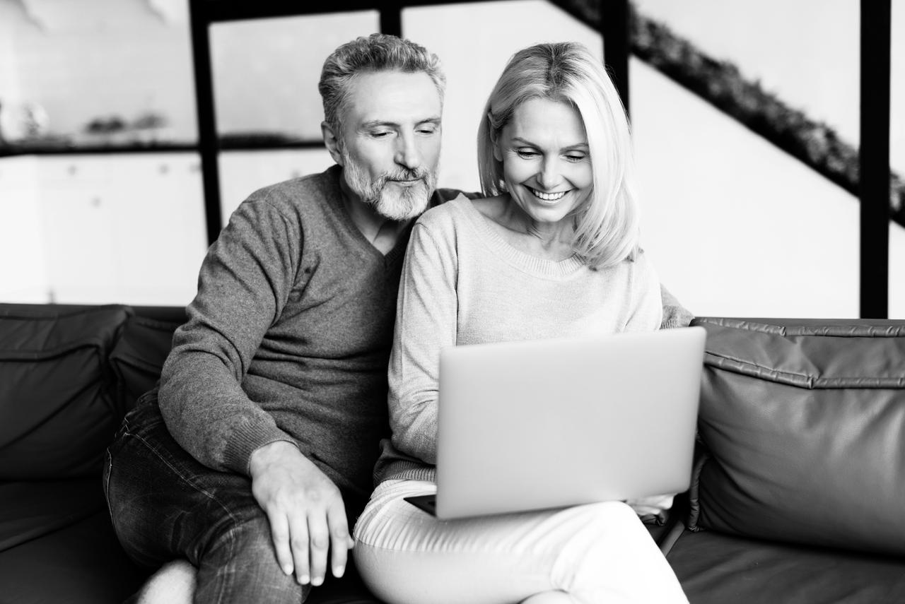 A woman and man sitting on the couch looking at a laptop