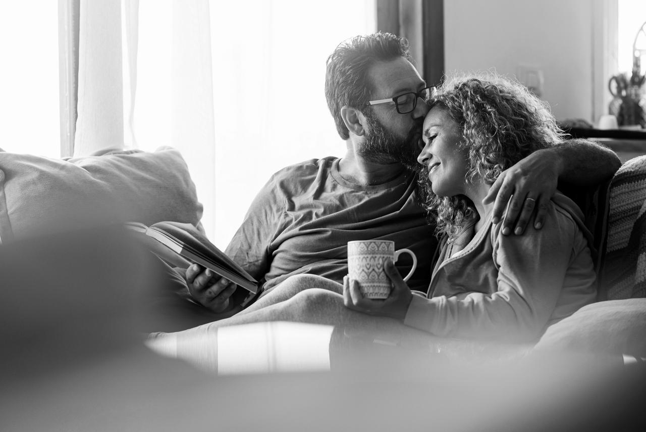 Male and female relax on the couch reading a book and drinking a tea