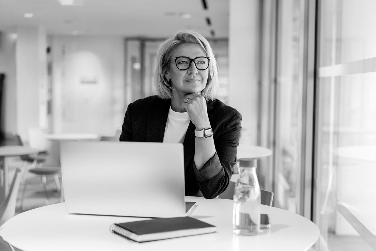 Businesswoman working on a laptop in an open space office looking out a window