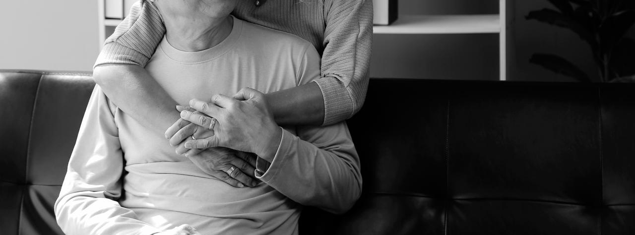 A man sitting on a couch being hugged from a person behind.