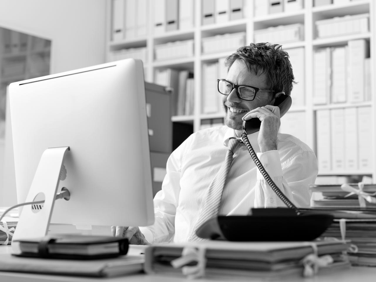 A businessman during a landline telephone call in the office A man talking on the telephone while sitting in front of a computer