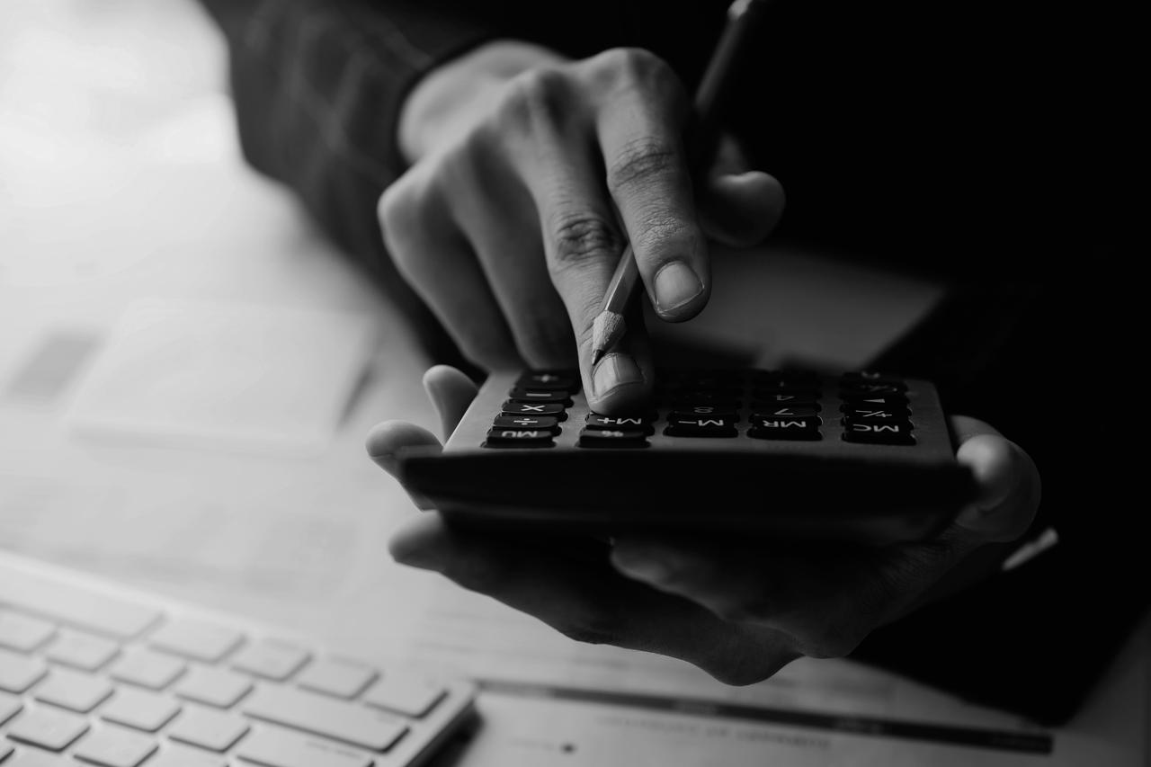 Hands holding a calculator and pencil while doing some calculations in front of a computer keyboard