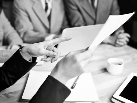 A hand is pointing at a paper document during a meeting