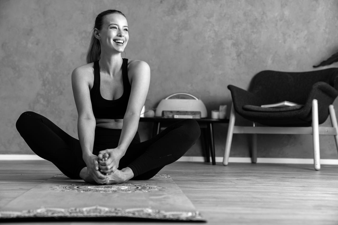 Smiling cheerful woman resting while sitting on yoga mat indoors