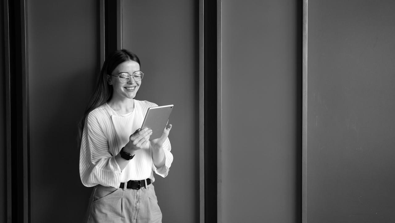 A young lady holding a tablet and standing against a wall