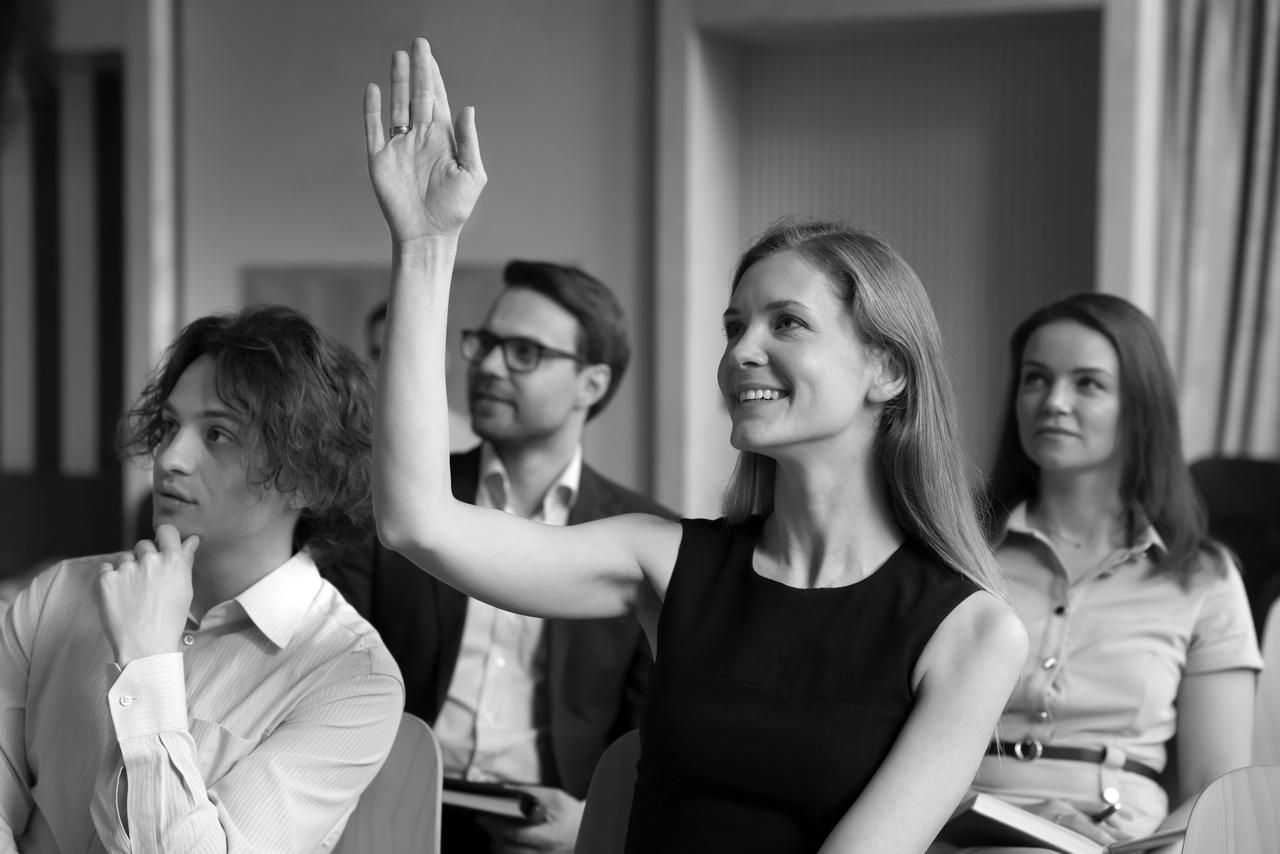 Smiling woman employee, educational seminar participant raise arm to ask question engaged in teambuilding activity