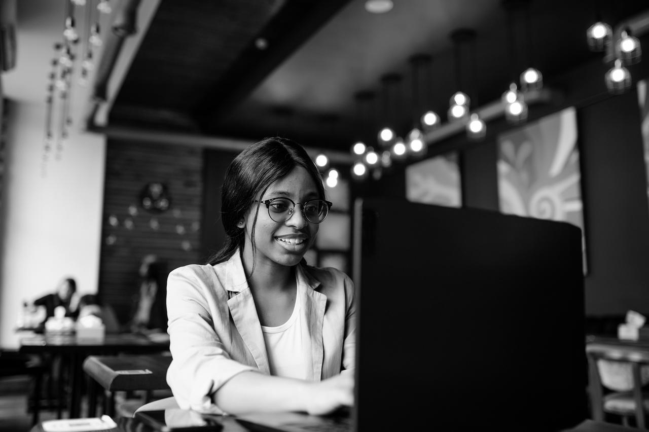 Young woman studying in front of a laptop and sitting in an open plan work area or cafe.