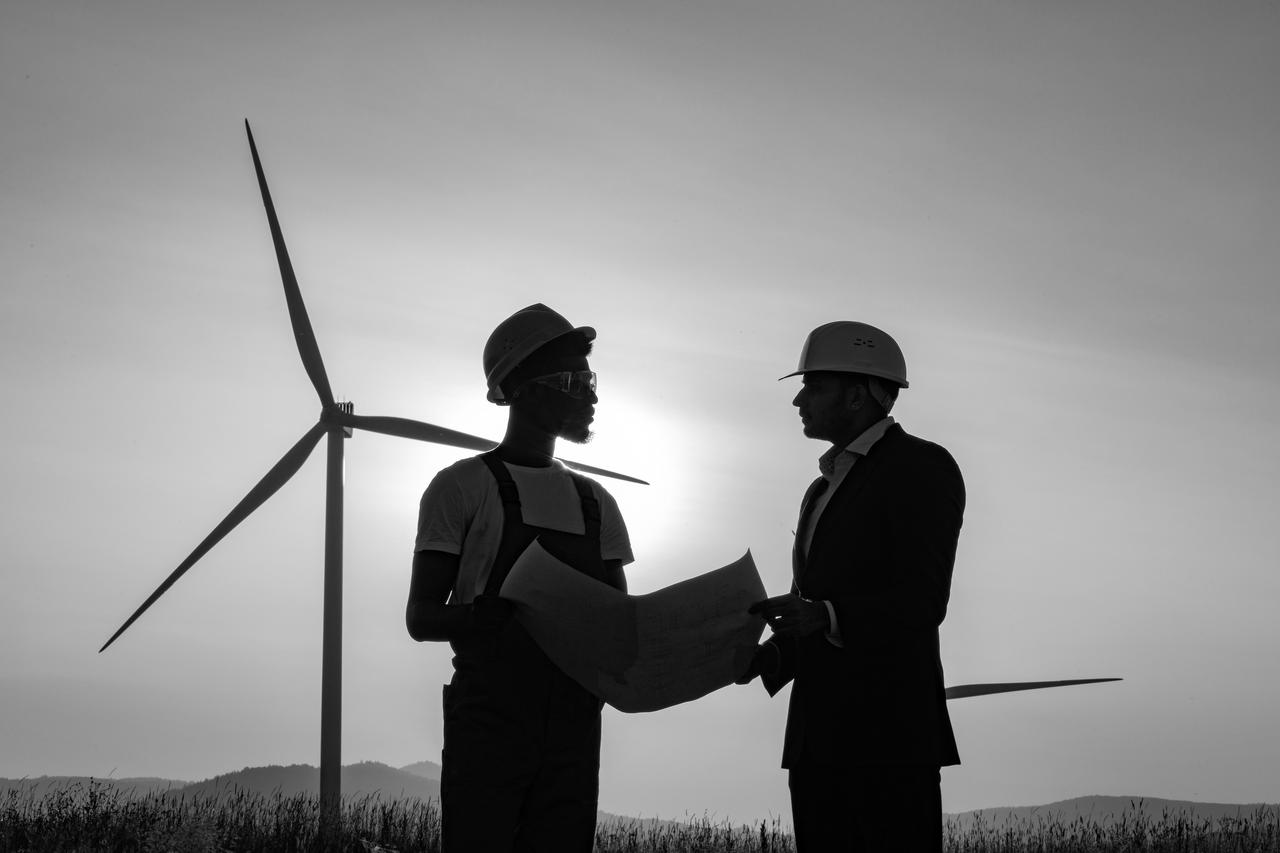 Two industrial workers talking in front of wind farm Two industrial workers examining wind turbines in rural area.