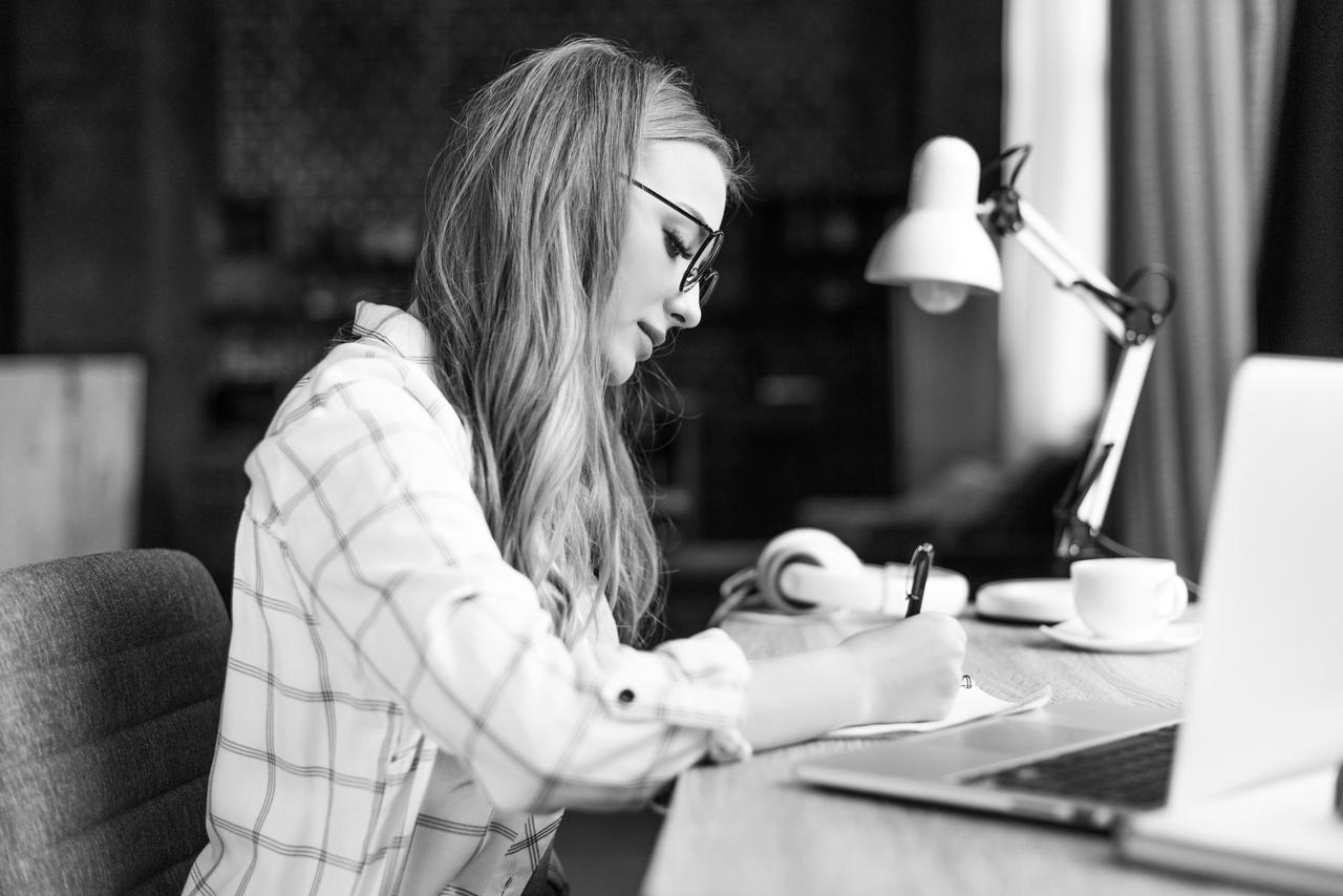 Young woman taking notes Concentrated young woman writing in notebook at workplace